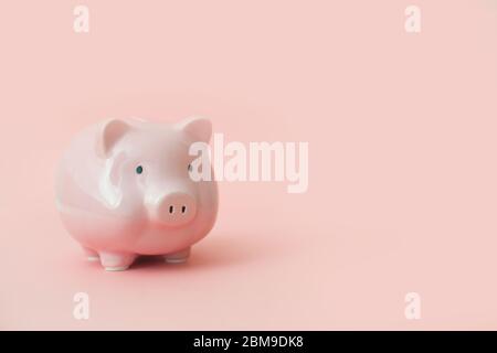 Sieben Sparschweine in verschiedenen Größen mit medizinischen Masken in absteigender Reihenfolge mit schwarzen Pfeil auf rosa Hintergrund aufgereiht. Konzept der finanziellen Stockfoto