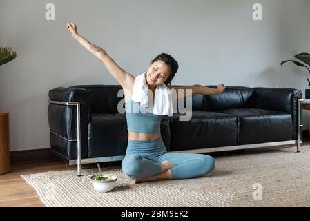 Eine junge Asiatin isst einen gesunden Gemüsesalat im Wohnzimmer