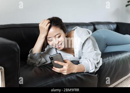 Eine junge Asiatin, die im Wohnzimmer Handy benutzt Stockfoto