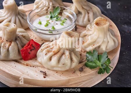 Gekocht traditionellen georgischen khinkali auf einem runden Holztablett mit Gewürzen, Petersilie und Sauce in der Mitte. Stockfoto