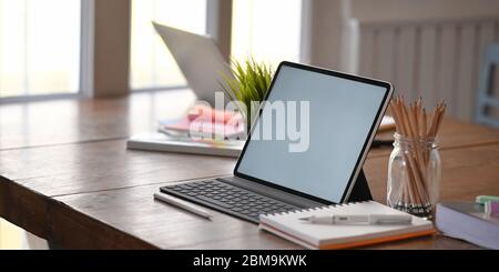 Foto von Computer-Tablet mit Tastatur-Fall setzen auf Holz Schreibtisch und umgeben von Bleistifthalter, Notebook, Topfpflanze, Stift und Laptop Ove Stockfoto