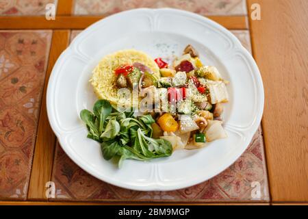 Weißer Teller mit gebratenen Pilzen und Gemüse, gekochtem Reis und frischem Spinat. Auf einer Holztafel mit Keramikfliesen verziert. Draufsicht Stockfoto