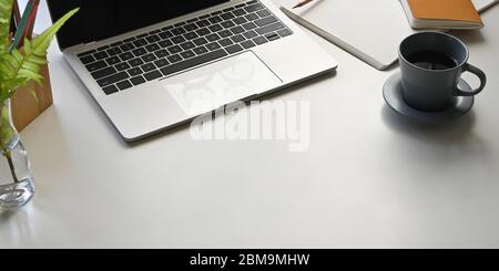 Foto von Computer-Laptop auf weißem Schreibtisch setzen und umgeben von Notebook, Tagebuch, Topfpflanze, Kaffeetasse und Bleistifthalter. Geordneter Arbeitsbereich Stockfoto