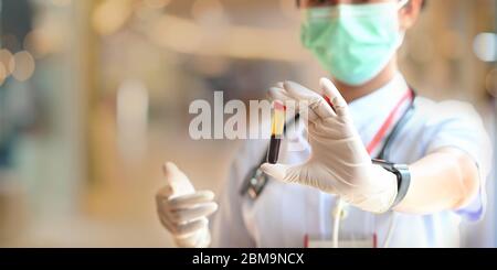 Foto von schönen Ärztin mit einer medizinischen Maske und Handschuh zeigt einen Blutschlauch für den Test während im modernen Untersuchungsraum über blu stehen Stockfoto