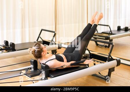 Frau, die die hundert Pilates Übung auf einem reformierten Bett in einem Fitnessstudio für die Stabilität der Kerns, Atmung und ein Herz-Kreislauf-Training Stockfoto