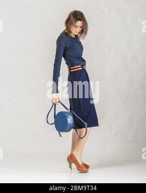 Stilvolle modische Frau trägt klassische blaue Langarm, Rock und braunen Absätzen halten trendige Leder rund blaue Handtasche. Kleidung und Accessoires Stockfoto