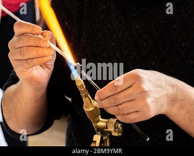 Die Hände des Handwerkers, der ein Glasthema des Handwerks macht. Glashersteller arbeiten geschmolzenes Glas mit einer flammenden Fackel. Nahaufnahme der Flamme von der Blasbrenner Stockfoto