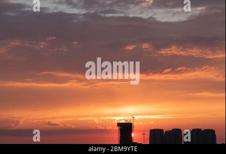 Bau- und Ski-Scraper-Gebäude und Kran gegen bunten Himmel mit Sonne. Baukonzept. Stockfoto