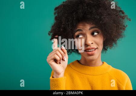 Porträt einer lächelnden jungen afrikanerin, die einen Pullover trägt, der isoliert auf grünem Hintergrund steht und flirtet Stockfoto