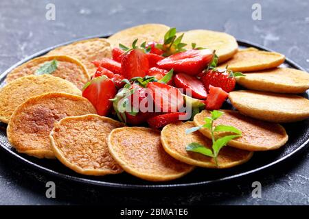 Süße frisch gebratene Haferflocken-Pfannkuchen mit Erdbeeren und Honig auf einem schwarzen Teller auf einem Betontisch, gesundes Essen, horizontale Ansicht von oben, schließen Stockfoto