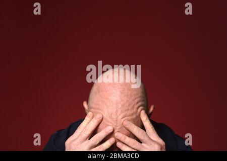 Kahlköpfiger Mann, der seinen Kopf mit Falten auf rotem Hintergrund berührt Stockfoto