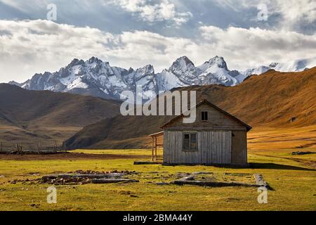 Alten rustikalen Holzhaus weiß im Tal mit Schnee Berggipfel in der Nähe von Kel Suu See in der naryn Region, Kirgisistan Stockfoto