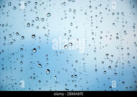 Tropfen Regen auf ein Fensterglas. Schöner blauer Wolkenhimmel im Hintergrund. Stockfoto