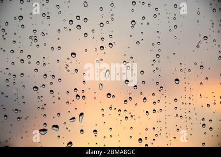 Tropfen Regen auf ein Fensterglas. Schöner, lebendiger Himmel im Hintergrund. Stockfoto