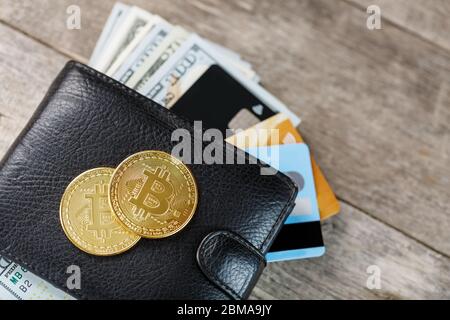 Schwarze Brieftasche mit Banknoten, elektronischen Karten und Bitcoins auf Holzhintergrund. Symbol für Wohlstand und Wohlstand. Nahaufnahme Stockfoto