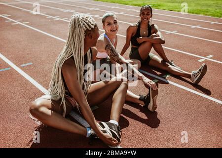 Glückliche Gruppe von weiblichen Athleten auf einer Laufstrecke sitzen und Stretching Beine. Frauen Läufer machen Aufwärmübungen im Stadion. Stockfoto