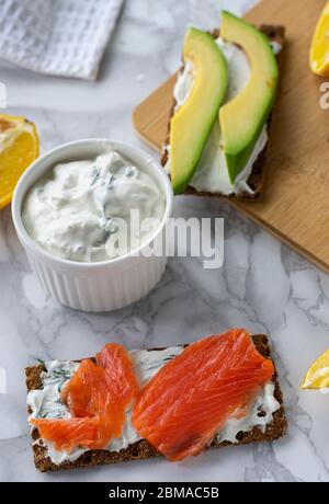 Frühstück am Morgen, zartes hausgemachtes Weichkäse auf Crackern mit geräucherter Forelle und Avocado Stockfoto