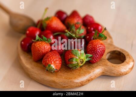 Gesunde und biologische rote Frühlingsfrüchte auf Holztisch mit natürlichem Licht, Erdbeeren, Kirschen, Himbeeren, alles frisch und reif, Basis einer Detox-Diät Stockfoto