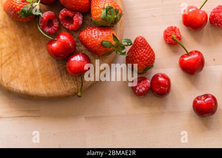 Gesunde und biologische rote Frühlingsfrüchte auf Holztisch mit natürlichem Licht, Erdbeeren, Kirschen, Himbeeren, alles frisch und reif, Basis einer gesunden Ernährung Stockfoto