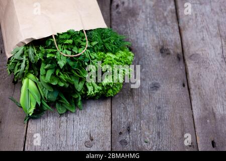 Frisches Gemüse in einem Papierbeutel - grüne Zwiebeln, Dill, Petersilie, Spinat, Rucola, Sauerampfer. Lieferung von Lebensmitteln und frischem Gemüse nach Hause. Holzhintergrund Stockfoto