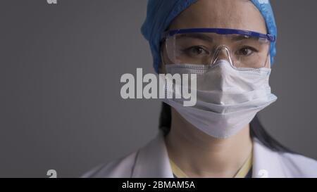 Besorgte Ärztin, die Kamera mit schützender medizinischer Uniform, Maske, Mütze und Brille anschaut. Asiatische Krankenschwester Gefühl Stress während der Pandemie. Schließen Stockfoto