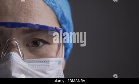 Müde Arzt schaut Kamera. Nahaufnahme eines medizinischen Auges. Ernste weibliche Krankenschwester mit Schutzmaske, Mütze und Schutzbrille. Speicherplatz kopieren bei Stockfoto