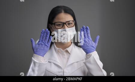 Müde Ärztin in weißer Uniform hob ihre Hände in Einweghandschuhen. Der Mediziner ist bereit, die Kranken zu retten. Medizin und Stockfoto