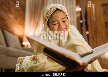 Schönes kleines Mädchen, das den koran liest und allein zu Hause einen muslimischen Hijab trägt Stockfoto