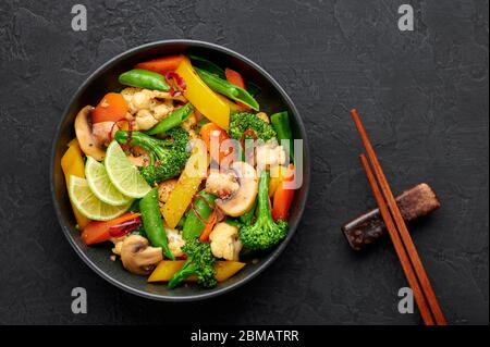 Pad Pak Ruam oder Veg Thai Stir-Fried Gemüse in schwarzer Schüssel auf dunklem Schiefer Hintergrund. Pad Pak ist thailand Küche vegetarisches Gericht mit Mischung aus Gemüse Stockfoto