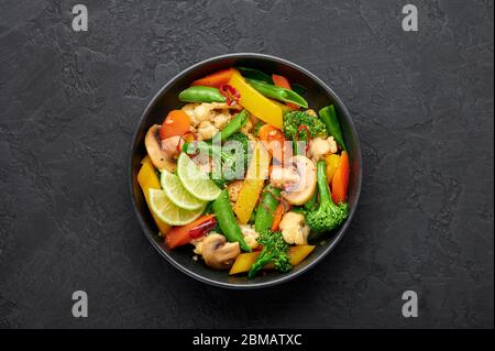 Pad Pak Ruam oder Veg Thai Stir-Fried Gemüse in schwarzer Schüssel auf dunklem Schiefer Hintergrund. Pad Pak ist thailand Küche vegetarisches Gericht mit Mischung aus Gemüse Stockfoto