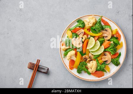 Pad Pak Ruam oder Veg Thai Stir-Fried Gemüse in weißem Teller auf grauem Beton Hintergrund. Pad Pak ist thailand Küche vegetarisches Gericht mit Mischung aus Gemüse Stockfoto