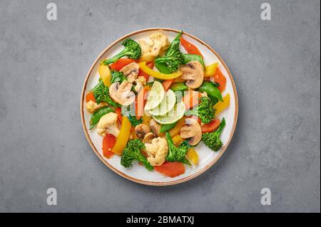 Pad Pak Ruam oder Veg Thai Stir-Fried Gemüse in weißem Teller auf grauem Beton Hintergrund. Pad Pak ist thailand Küche vegetarisches Gericht mit Mischung aus Gemüse Stockfoto