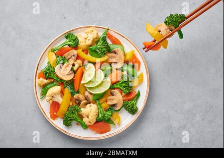 Pad Pak Ruam oder Veg Thai Stir-Fried Gemüse in weißem Teller auf grauem Beton Hintergrund. Pad Pak ist thailand Küche vegetarisches Gericht mit Mischung aus Gemüse Stockfoto