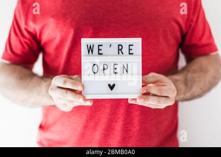 Ende der Quarantäne. Mann mit Leuchtkasten mit Grußtext Wir sind offen in seinen Händen. Hotel, Café, lokaler Shop, Service-Besitzer begrüßen Gäste af Stockfoto