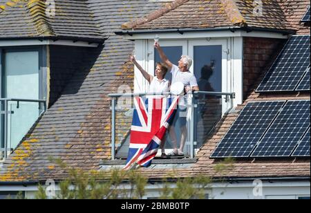 Littlehampton UK 8. Mai 2020 - EIN Paar auf seinem Balkon in Ferring bei Worthing erhebt ein Glas zum Gedenken an den Jahrestag des VE Day während der Sperrbeschränkungen der COVID-19-Pandemie. Es ist 75 Jahre her, dass der Sieg in Europa über die Deutschen während des Zweiten Weltkriegs verkündet wurde : Credit Simon Dack / Alamy Live News Stockfoto