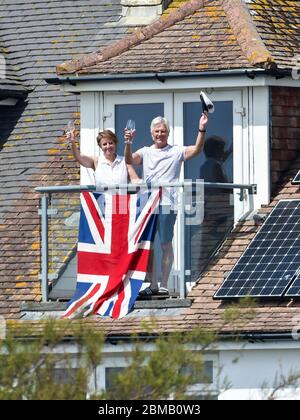 Littlehampton UK 8. Mai 2020 - EIN Paar auf seinem Balkon in Ferring bei Worthing erhebt ein Glas zum Gedenken an den Jahrestag des VE Day während der Sperrbeschränkungen der COVID-19-Pandemie. Es ist 75 Jahre her, dass der Sieg in Europa über die Deutschen während des Zweiten Weltkriegs verkündet wurde : Credit Simon Dack / Alamy Live News Stockfoto