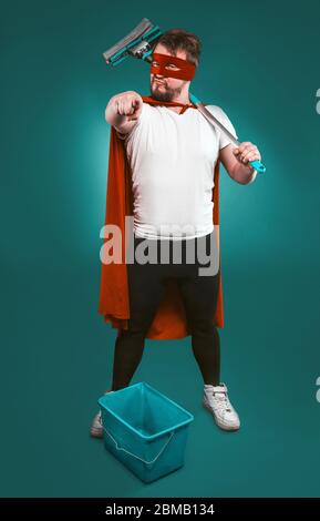 Superheld ist bereit, für Sauberkeit zu kämpfen, tapferer Mann in einer roten Superhelden Uniform mit einem Eimer und einem Mopp zeigt die Kamera mit seinem Zeigefinger Stockfoto