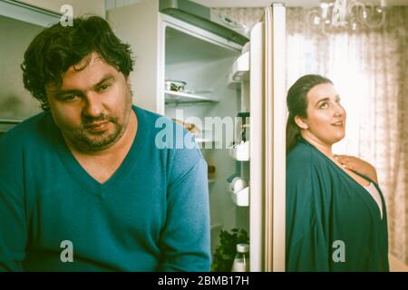 Ein wohlüberlegtes, körperpositives Paar steht in der Küche neben dem offenen Kühlschrank Stockfoto