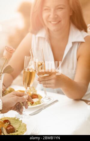 Glückliche Frau lächelt mit einem Glas Weißwein. Ältere Paare haben Veranstaltung im Freien am Strand Café. Selektiver Fokus auf menschliche Hände mit Gläsern Wein Stockfoto