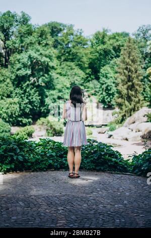 Sofia Park, Ukraine. Junges Mädchen in einem schönen Sommerpark. Brunette Mädchen in einem farbigen Sonnenkleid. Mädchen Tourist auf der Aussichtsplattform im Park Stockfoto