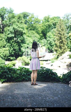 Sofia Park, Ukraine. Junges Mädchen in einem schönen Sommerpark. Mädchen in einem farbigen Sonnenkleid mit einer touristischen Karte. Frau mit einer touristischen Karte auf der Beobachtung Stockfoto