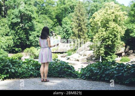 Sofia Park, Ukraine. Junges Mädchen in einem schönen Sommerpark. Mädchen in einem farbigen Sonnenkleid mit einer touristischen Karte. Frau mit einer touristischen Karte auf der Beobachtung Stockfoto