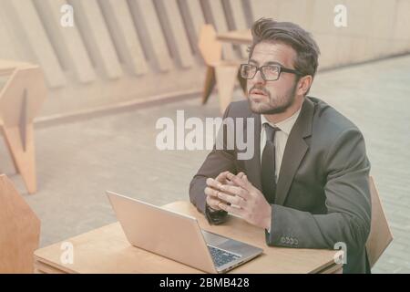 Geschäftsmann arbeitet Laptop auf der Straße im Freien. Intelligenter junger Mann, der an der frischen Luft am Tisch sitzt und über eine Strategie zur Geschäftsentwicklung nachdenkt Stockfoto