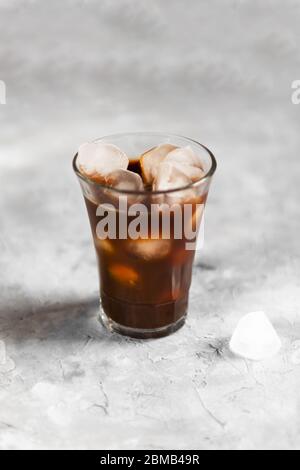 Ice Black Brühen Sie Kaffee in hohem Glas mit Eisstücken auf einem grauen dunklen Hintergrund, Nahaufnahme, natürliches Licht, frisches Sommergetränk Stockfoto