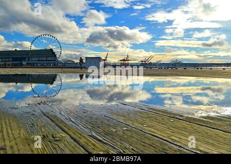 Seattle 2013, eine Wasserpfütze in einem Holzboden spiegelt den Himmel und die Wolken, die Hafenkulisse im Hintergrund unter einem hellen Himmel Stockfoto
