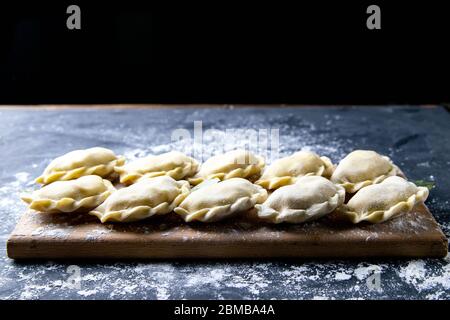 Roher Knödel mit Kartoffeln. Vorbereitung Knödel auf einem Holzbrett auf dunklem Hintergrund. Draufsicht, Nahaufnahme Stockfoto