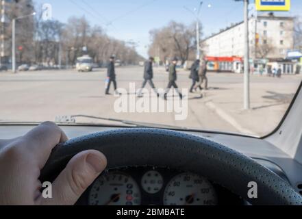 Blick aus dem Auto, Hand des Mannes am Lenkrad des Autos, befindet sich gegenüber der Fußgängerampel und Fußgänger über die Straße Stockfoto