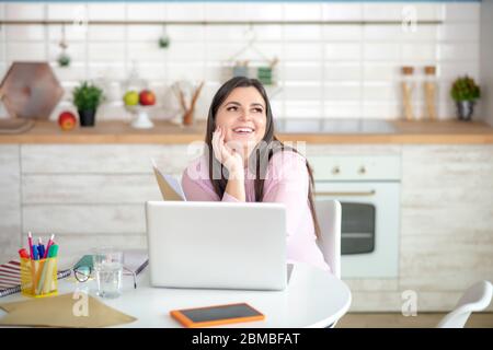 Junge Frau in einer rosa Bluse sitzt am Tisch und sieht verträumt Stockfoto
