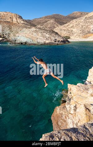 Ein Mann, der von einem Felsen ins Meer in der Nähe von Livadaki Beach, Folegandros, Kykladen Inseln, Griechenland springt Stockfoto