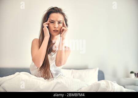 Kaukasische besorgte Frau mit Kopfschmerzen auf weichem Bett sitzen Stockfoto